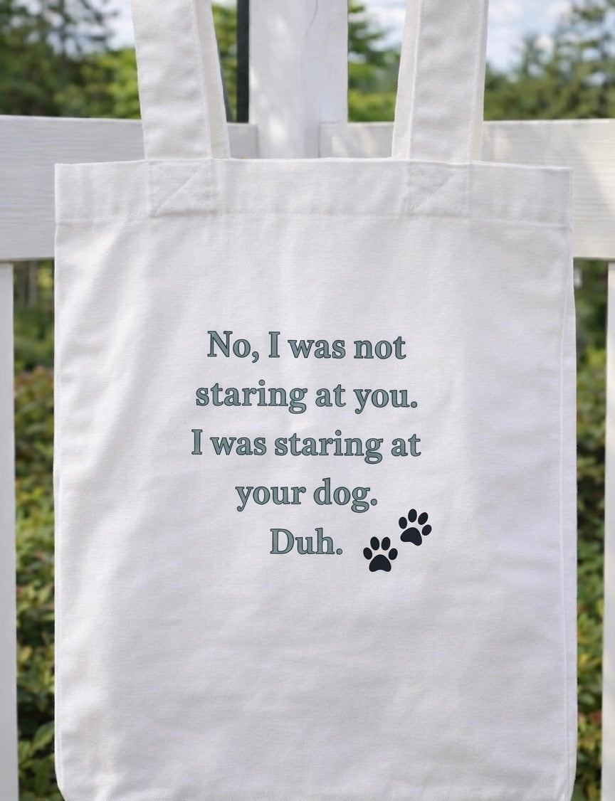 White tote bag with humorous text reading "No, I was not staring at you. I was staring at your dog. Duh." and paw print on a white background